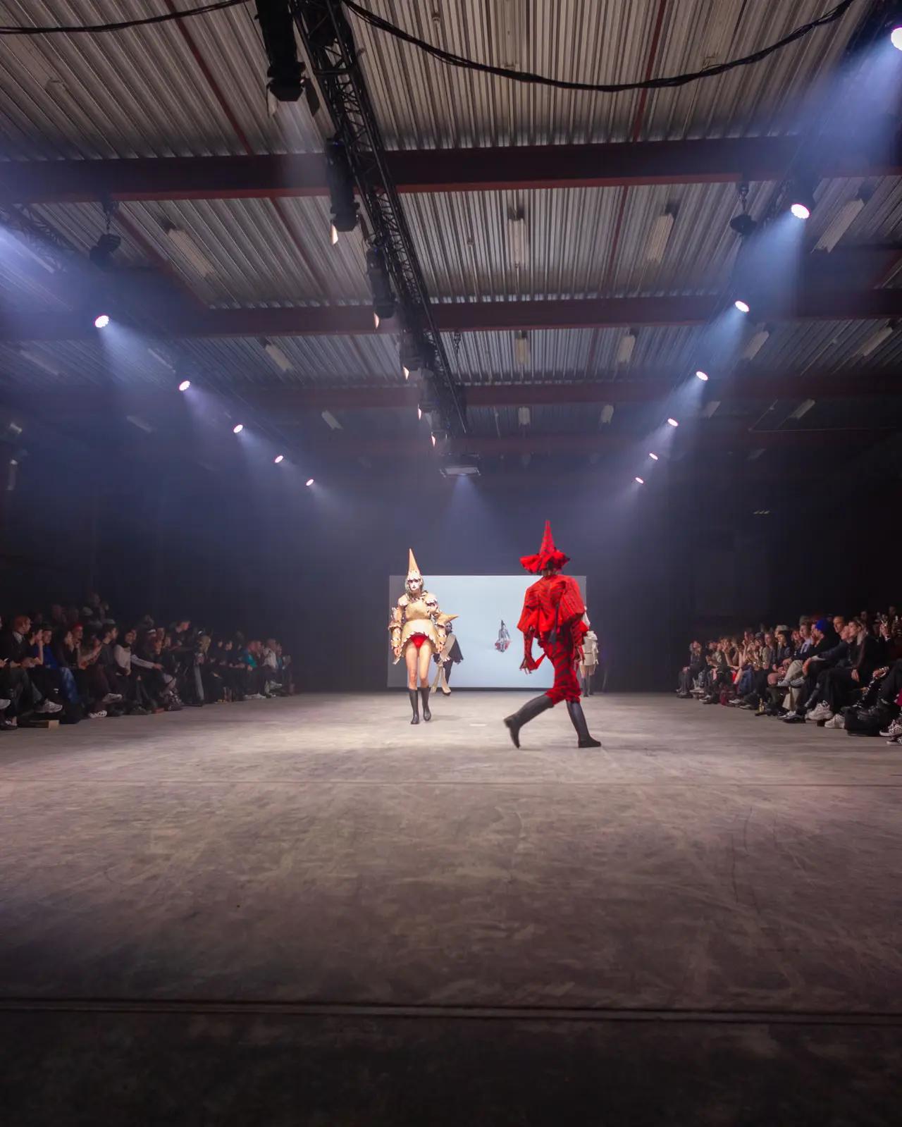 Fashion show in a hall at Door Open Space, two models on a lit runway